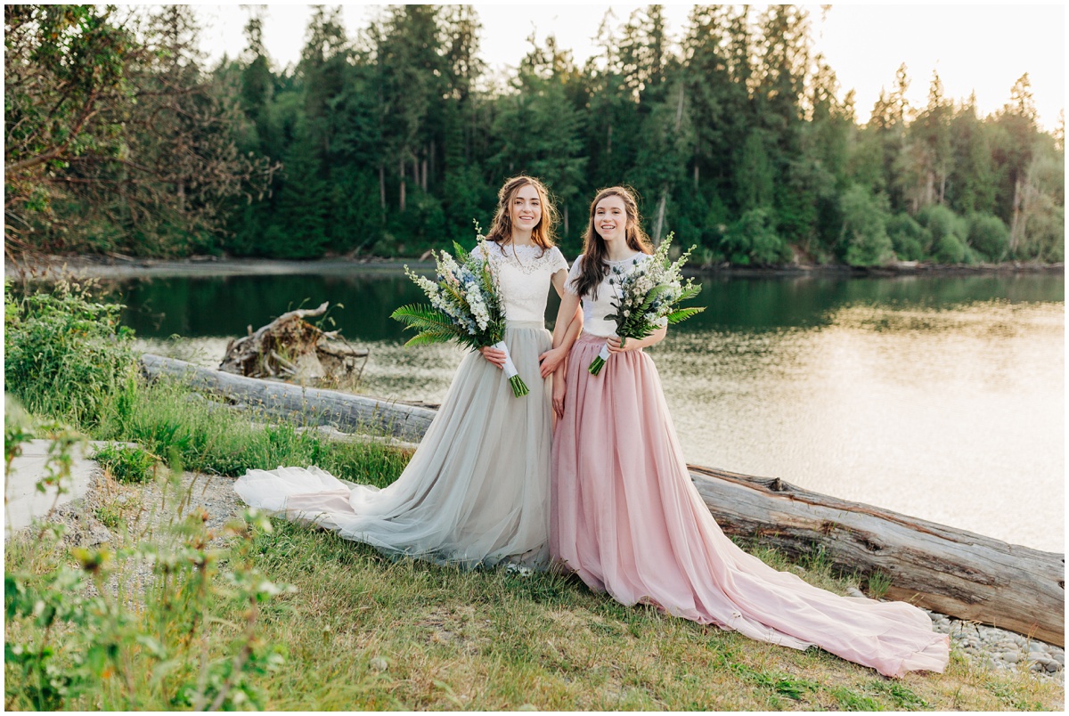 two brides pose with long dress on grass by sound bay