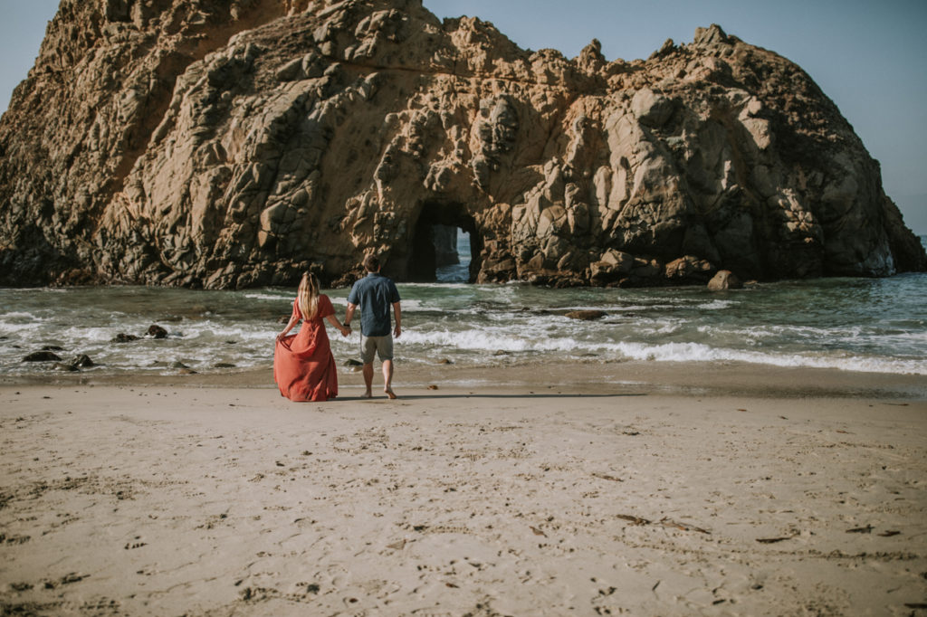 couple walking on beach with keyhole arch