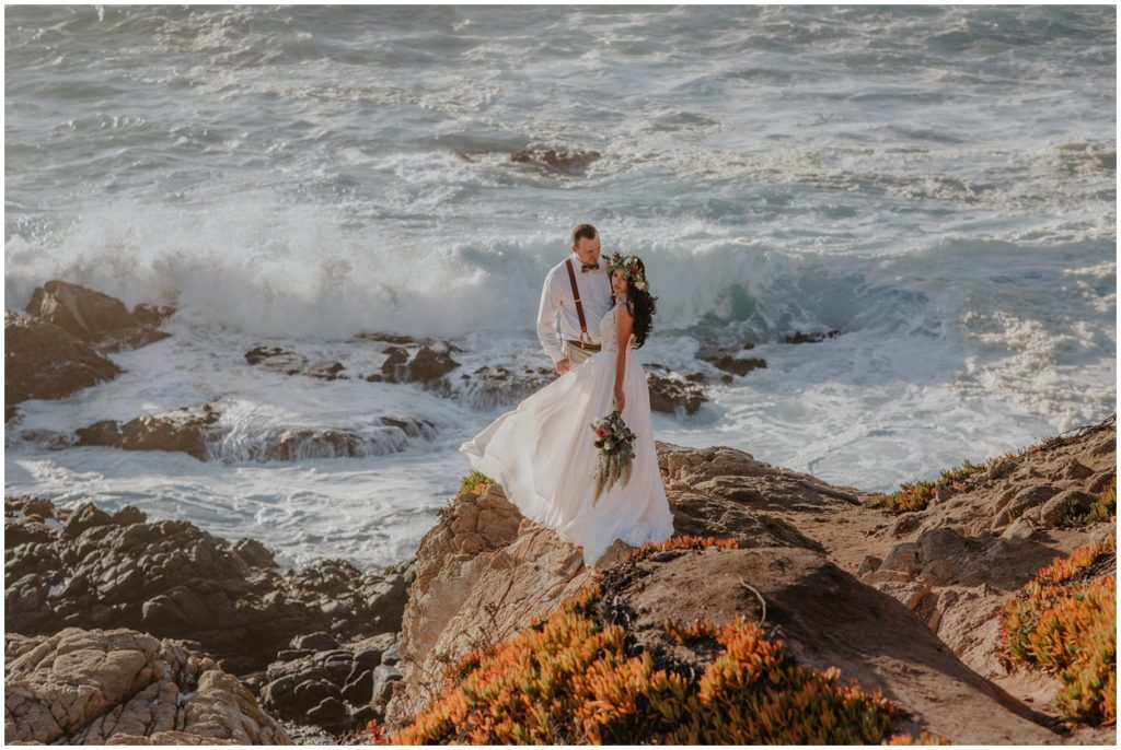 married couple standing on big sur rocks by ocean
