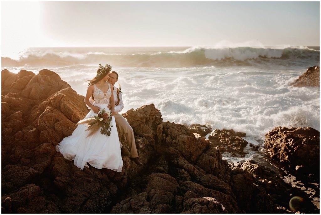bride and groom sitting by the ocean 