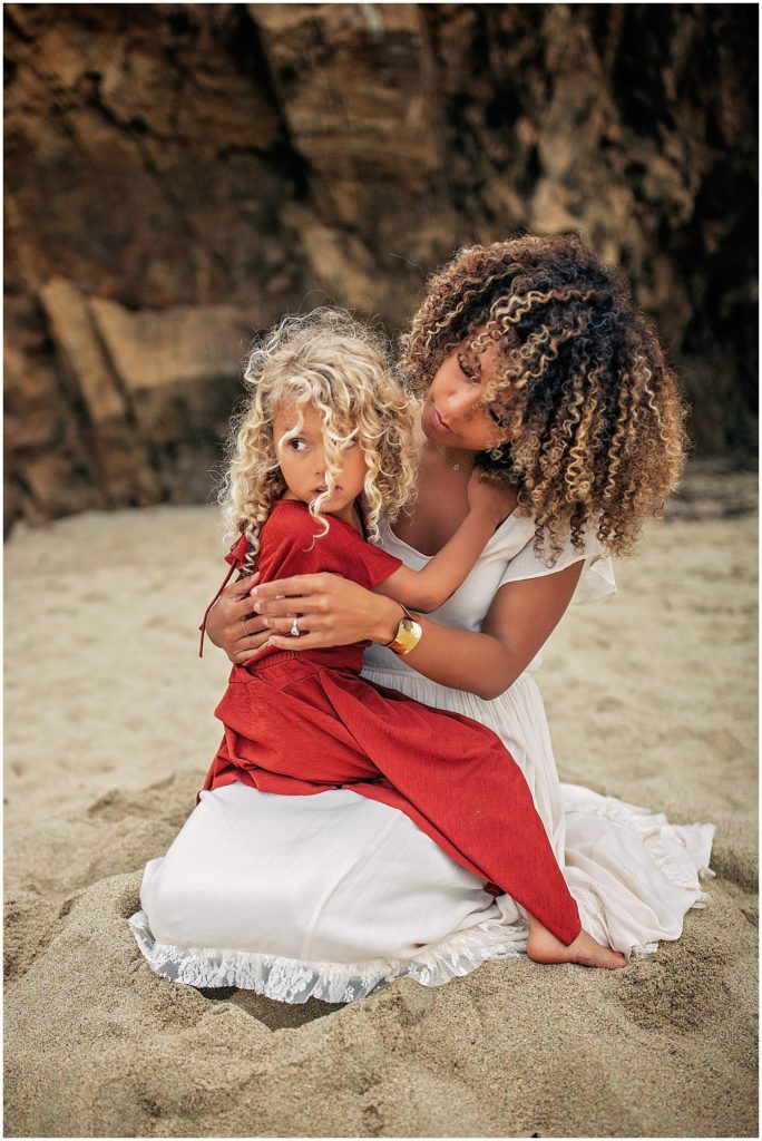 mother comforting girl with curly hair on beach