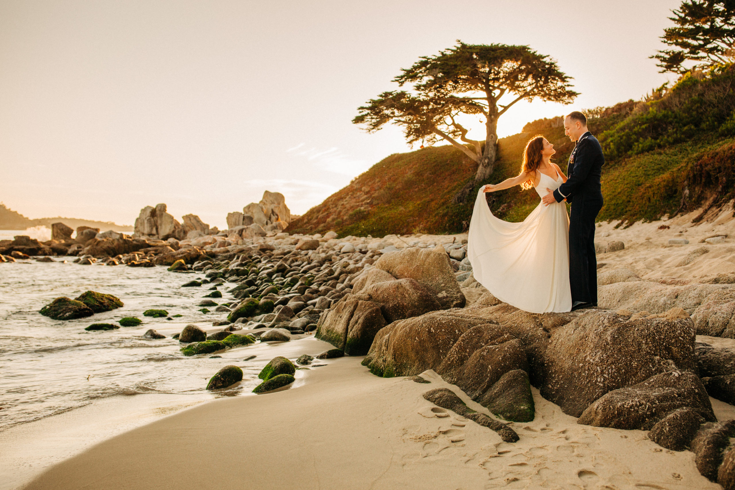 bride and groom standing on rocks at sunset