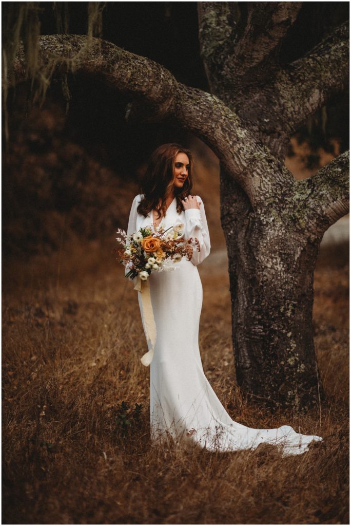 bride standing by tree and holding bouquet