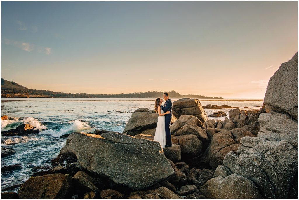 bride and groom standing on rocks at carmel beach at sunset