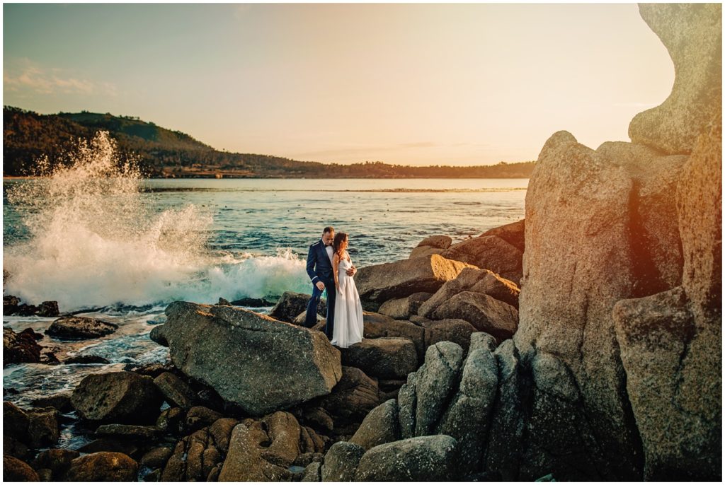 couple standing on rocks by the ocean at sunset